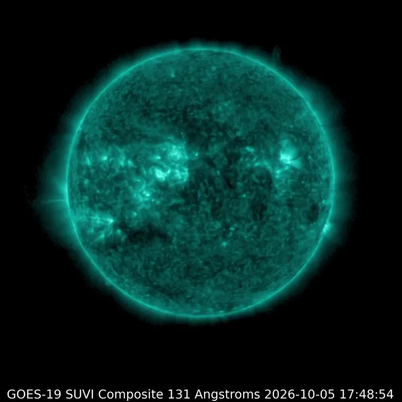 The sun is glowing teal in extreme ultraviolet light, with bright flashes from flares in active regions near the center.