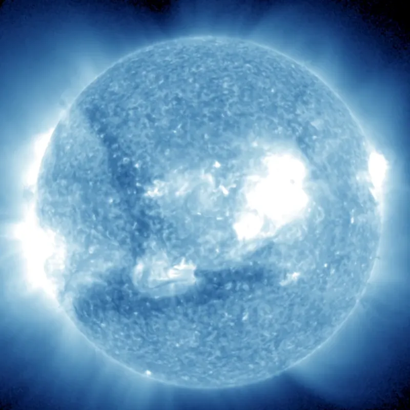 The sun glowing blue in extreme ultraviolet light, as a bright flare sends a faint wave rippling across the disk.