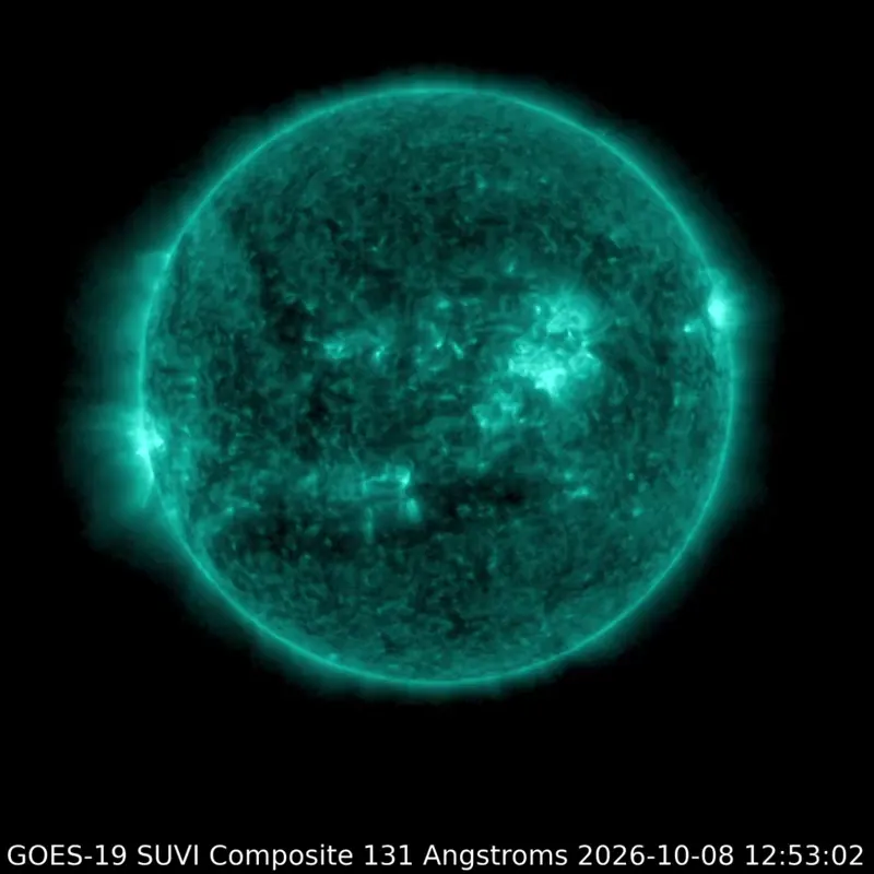 The sun glowing teal in extreme ultraviolet light, with a bright flash erupting from a large active region.