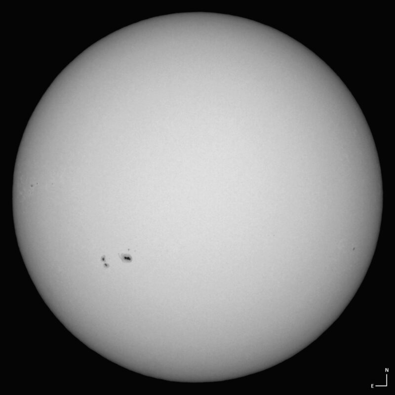 The sun, seen as a large white sphere with small dark spots.