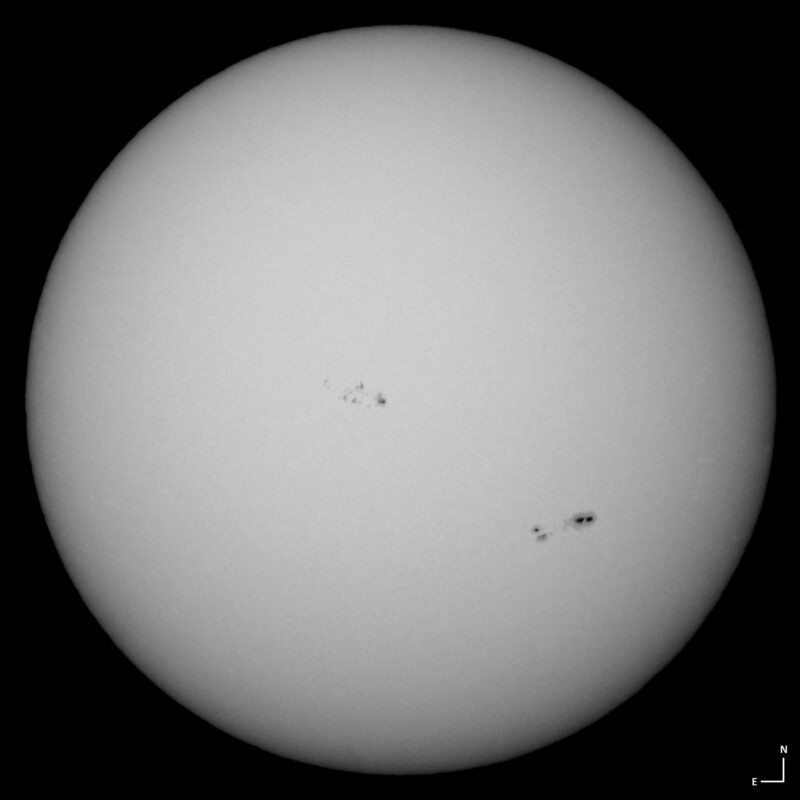 The sun, seen as a large white sphere with small dark spots.