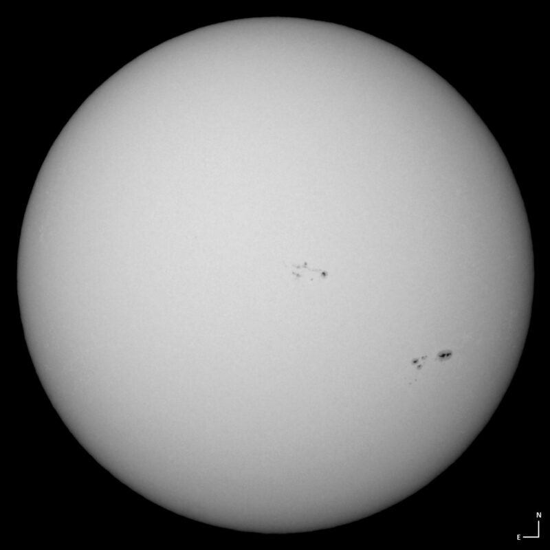 The sun, seen as a large white sphere with small dark spots.