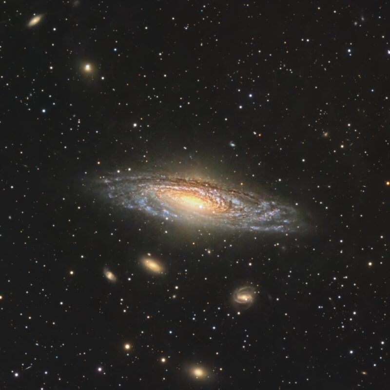 Large, yewllowish galaxy, a spiral seen almost edge-on, with a foreground of numerous stars.