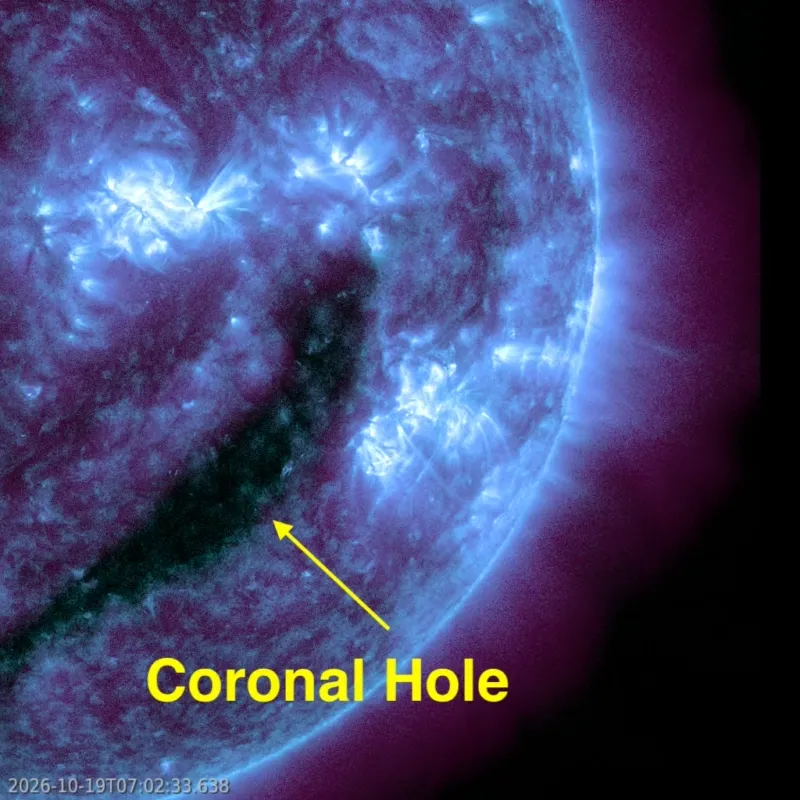Close-up of the sun in blue and purple ultraviolet light, showing a long dark coronal hole and a bright flare nearby.